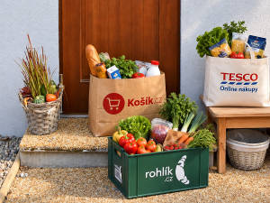 Vizualizace nákupních tašek a boxů z Košíku, Tesca a Rohliku před reálným zápražím domu.